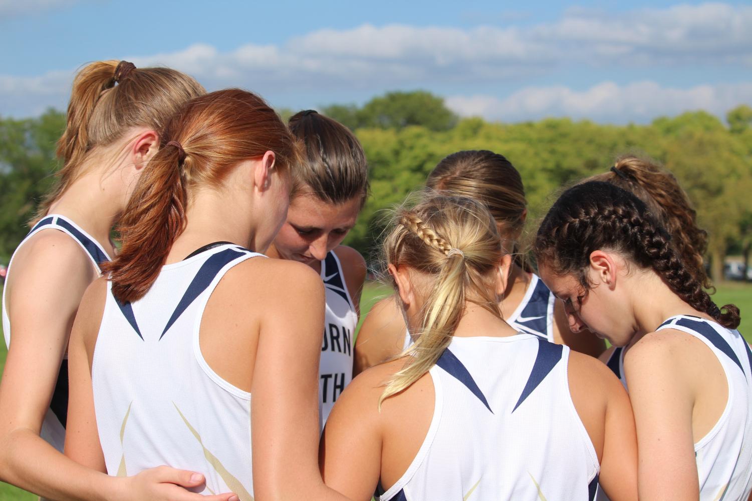 In this together: Varsity girls’ cross country huddles up before a run. The team supports each other on and off the course, as they help motivate each other.